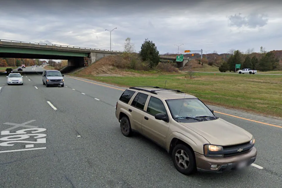 A two-lane highway cuts through a small canyon. The photo is taken from the perspective of a vehicle on the road.